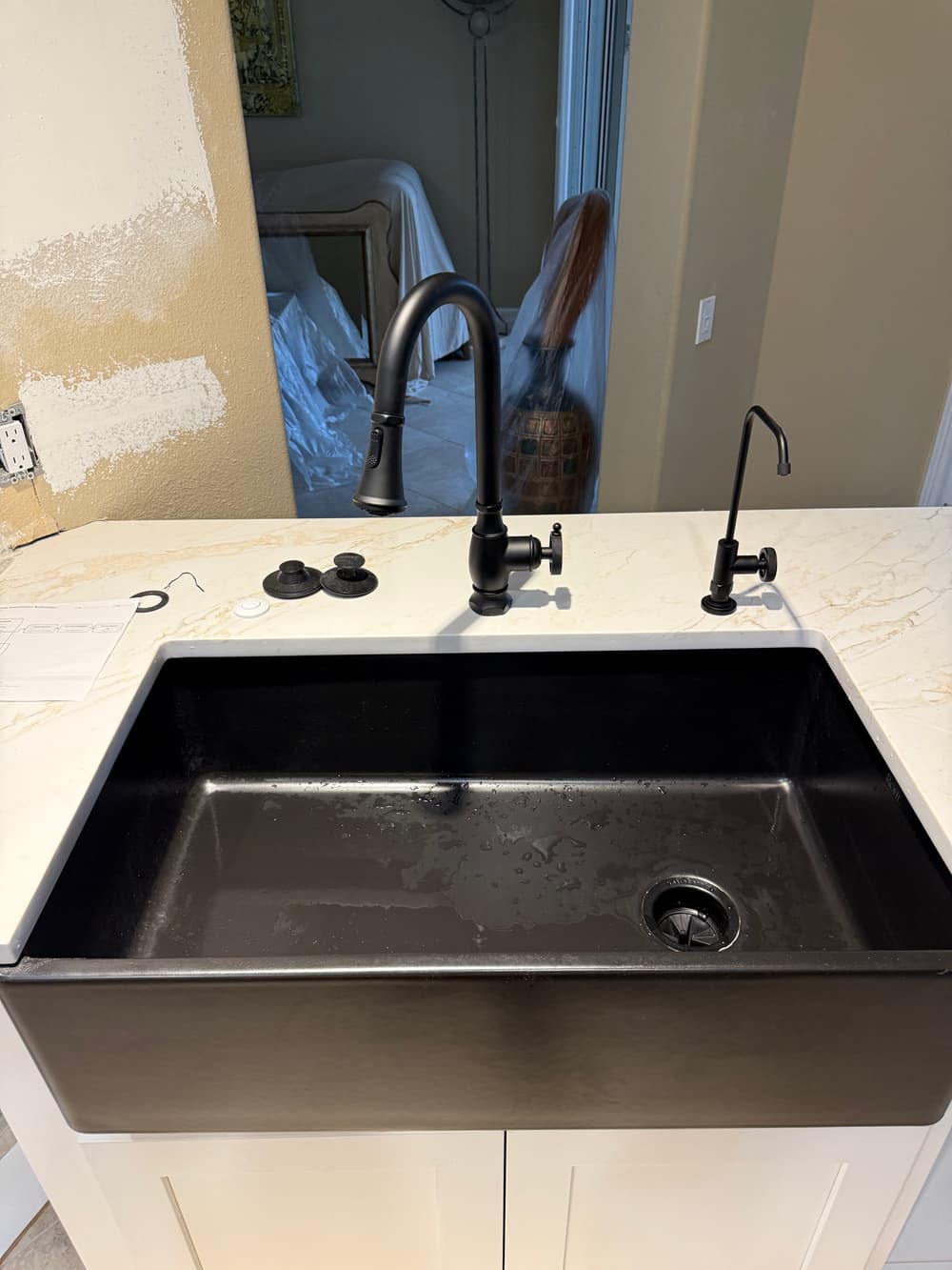 Black farmhouse sink with modern faucet and pull-down sprayer on marble countertop.
